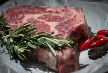 Close-up of a raw steak garnished with rosemary and chilies, ideal for cooking concepts.